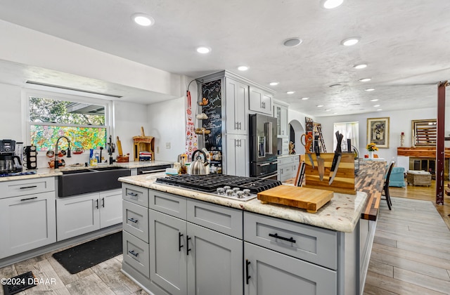 kitchen with gray cabinetry, sink, light hardwood / wood-style flooring, light stone counters, and stainless steel appliances