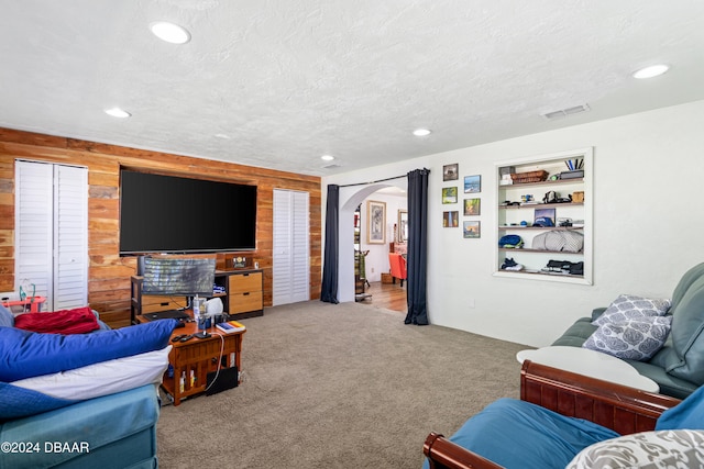 living room with carpet, built in features, a textured ceiling, and wooden walls