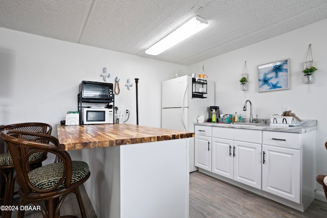 kitchen featuring sink, light wood-type flooring, a textured ceiling, butcher block countertops, and white cabinetry