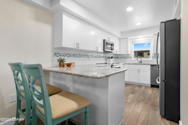 kitchen with kitchen peninsula, appliances with stainless steel finishes, decorative backsplash, light stone countertops, and light hardwood / wood-style floors