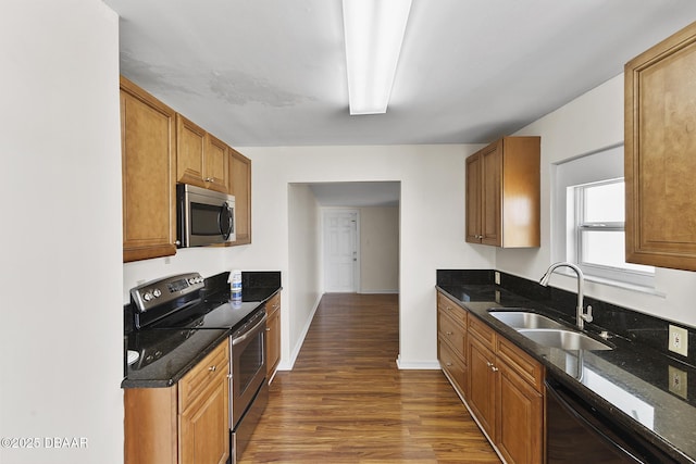 kitchen with dark wood finished floors, brown cabinetry, appliances with stainless steel finishes, and a sink