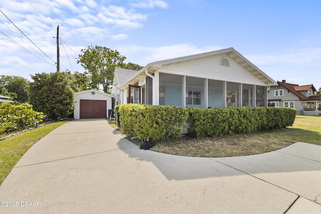 view of front of house featuring an outbuilding, a sunroom, a detached garage, and concrete driveway