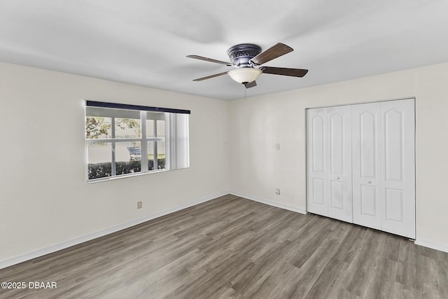unfurnished bedroom with baseboards, wood finished floors, ceiling fan, and a closet