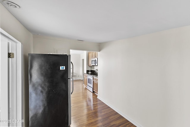 kitchen with dark wood-type flooring, stainless steel appliances, and baseboards