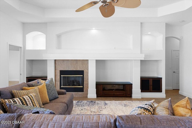 living room featuring a high ceiling, ceiling fan, a tile fireplace, and built in shelves