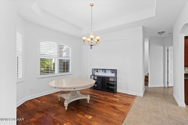 dining area featuring an inviting chandelier, a tray ceiling, and wood-type flooring