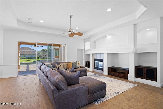 living room featuring light tile patterned floors, a tray ceiling, a tile fireplace, and ceiling fan