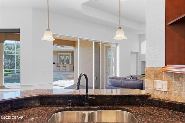 kitchen with dark stone counters, hanging light fixtures, sink, and backsplash