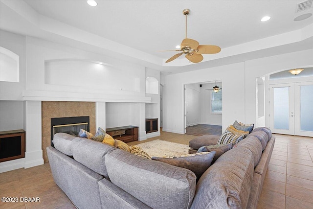 tiled living room featuring a fireplace, ceiling fan, french doors, and a tray ceiling