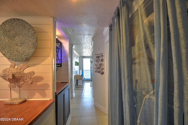 corridor with light tile patterned floors, a textured ceiling, and ornamental molding