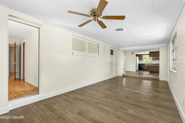 unfurnished living room featuring dark hardwood / wood-style flooring, crown molding, and ceiling fan