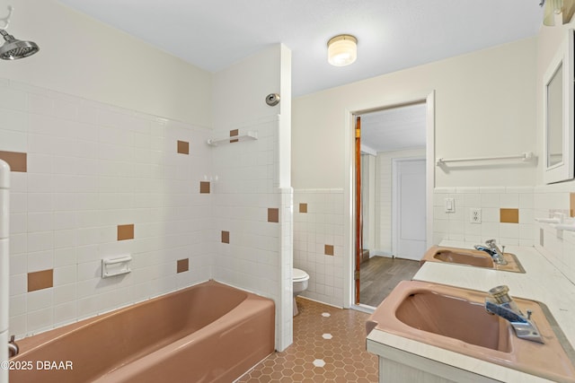 full bathroom with tile walls, tile patterned flooring, tiled shower / bath combo, vanity, and toilet