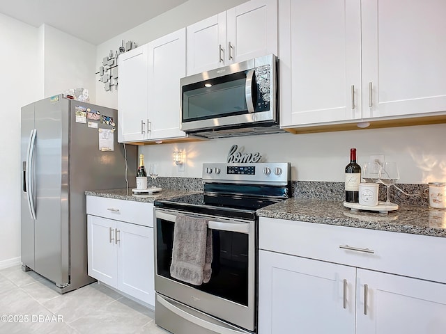 kitchen with appliances with stainless steel finishes, white cabinetry, dark stone counters, and light tile patterned flooring