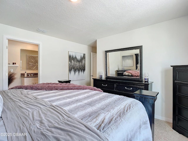 bedroom with a textured ceiling, ensuite bathroom, and light carpet