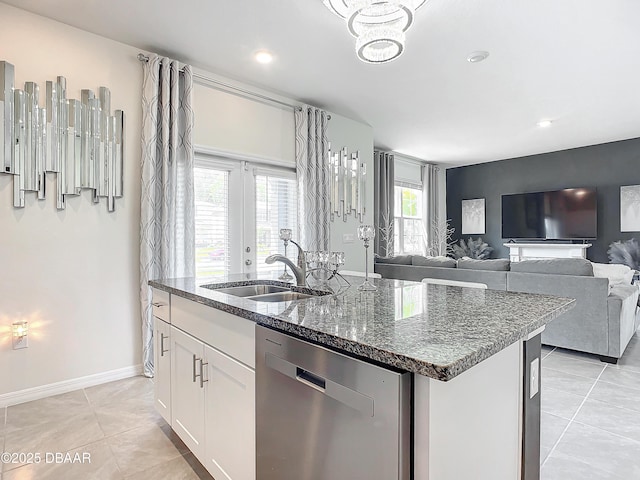 kitchen with a kitchen island with sink, white cabinets, sink, stainless steel dishwasher, and dark stone countertops