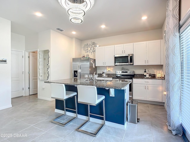 kitchen with dark stone counters, stainless steel appliances, white cabinetry, and a center island with sink