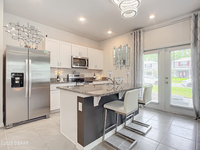 kitchen featuring dark stone countertops, white cabinetry, an island with sink, and stainless steel appliances