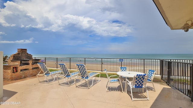 view of patio featuring an outdoor stone fireplace, a water view, and a beach view