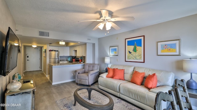 living room featuring light hardwood / wood-style flooring, a textured ceiling, and ceiling fan