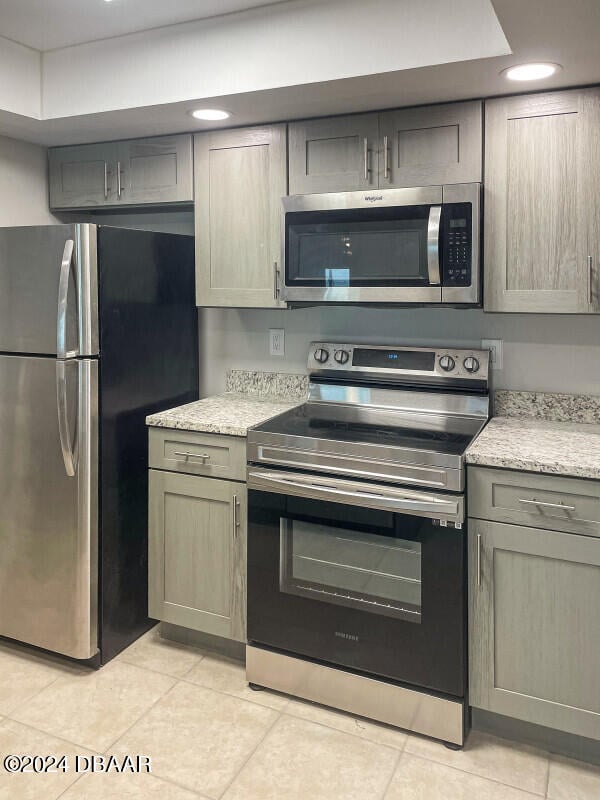 kitchen with appliances with stainless steel finishes, light tile patterned flooring, and light stone countertops