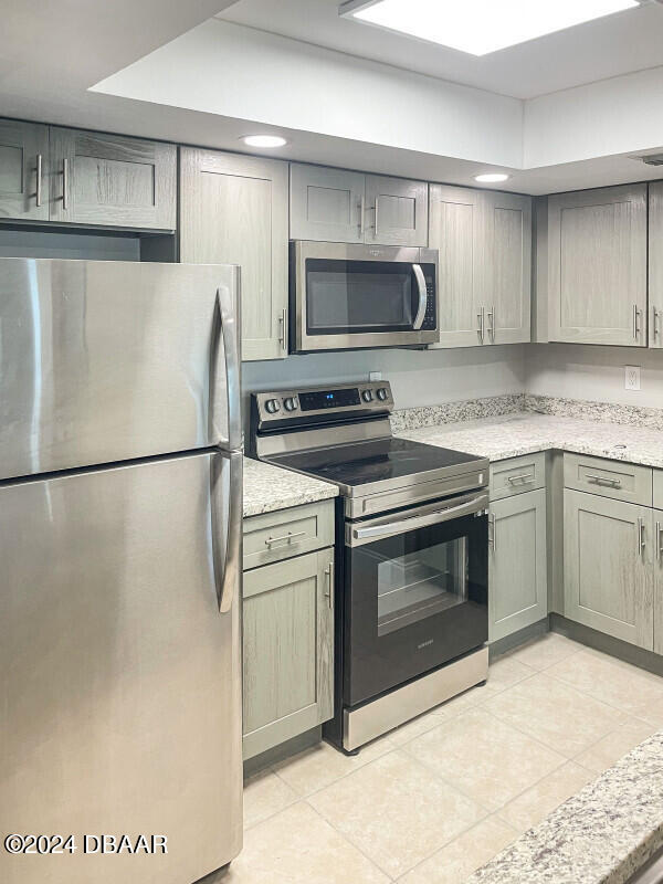 kitchen with gray cabinets, light stone countertops, light tile patterned flooring, and stainless steel appliances