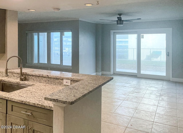 kitchen featuring light tile patterned floors, light stone countertops, sink, kitchen peninsula, and ceiling fan