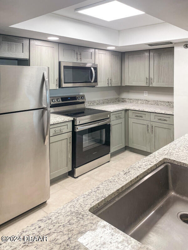 kitchen featuring appliances with stainless steel finishes, light tile patterned flooring, and light stone counters