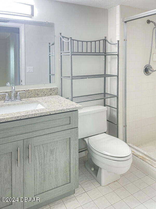 bathroom with a shower with door, vanity, toilet, and tile patterned floors