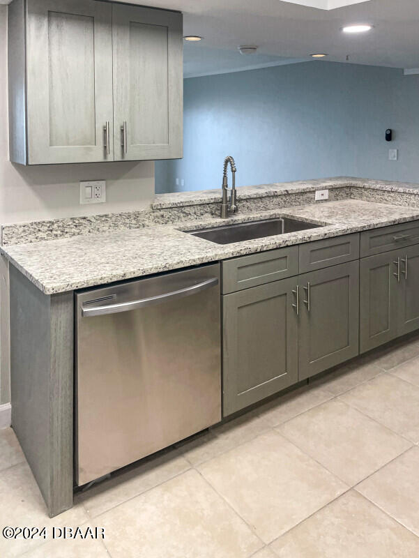 kitchen featuring stainless steel dishwasher, gray cabinets, sink, and light stone counters