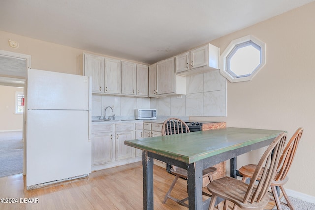 kitchen with decorative backsplash, white appliances, sink, and light hardwood / wood-style floors