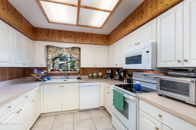 kitchen featuring white appliances, white cabinetry, sink, wood walls, and light tile patterned floors