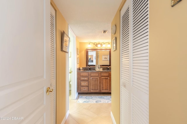 hallway featuring visible vents, a sink, and light tile patterned flooring