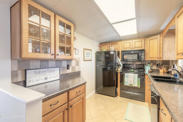 kitchen with a sink, a paneled ceiling, light tile patterned floors, tasteful backsplash, and black appliances