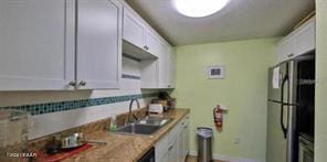 kitchen featuring stainless steel fridge, white cabinetry, and sink