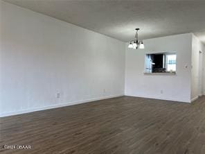 spare room featuring a notable chandelier and dark wood-type flooring