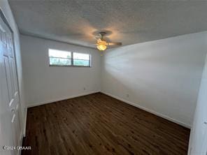 empty room with a textured ceiling, dark wood-type flooring, and ceiling fan