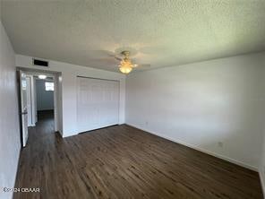 unfurnished bedroom with a textured ceiling, dark wood-type flooring, ceiling fan, and a closet