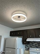 kitchen with dark brown cabinets, tasteful backsplash, a textured ceiling, and white appliances