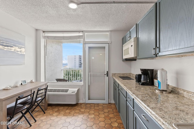 kitchen featuring gray cabinets, light stone counters, a wall mounted AC, and a textured ceiling