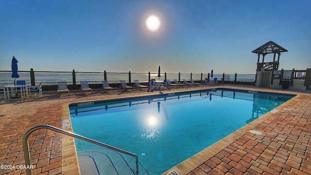 pool at dusk with a water view and a patio area