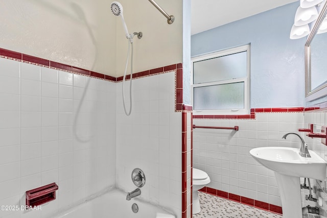 bathroom featuring shower / washtub combination, a wainscoted wall, tile walls, toilet, and a sink