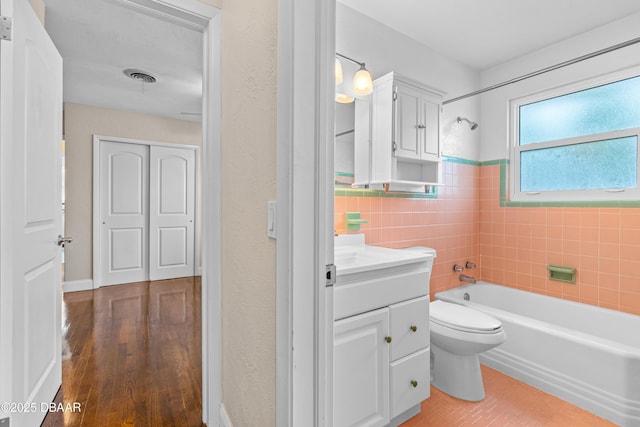 bathroom featuring bathing tub / shower combination, tile walls, visible vents, toilet, and vanity