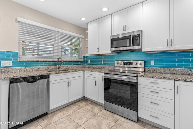 kitchen featuring stainless steel appliances, white cabinets, a sink, and light stone countertops