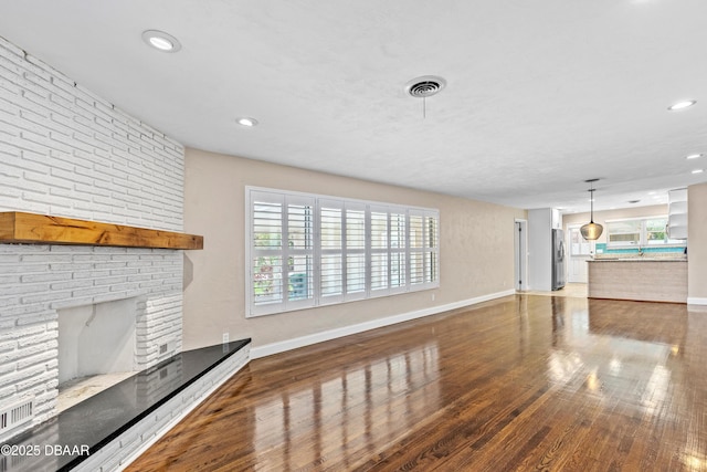 unfurnished living room with a brick fireplace, baseboards, wood finished floors, and recessed lighting