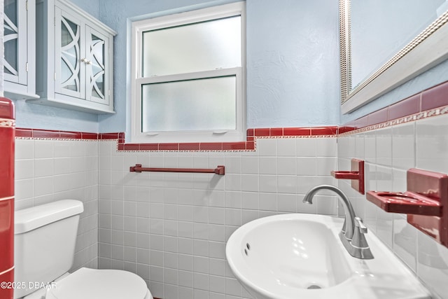 bathroom with toilet, tile walls, a sink, and a textured wall