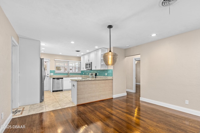 kitchen with a peninsula, light wood-style flooring, appliances with stainless steel finishes, and white cabinets