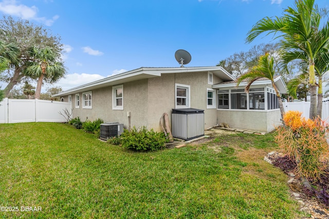 rear view of property featuring central AC unit, a fenced backyard, a sunroom, a lawn, and stucco siding