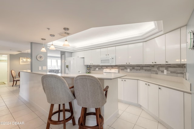 kitchen featuring white appliances, hanging light fixtures, a tray ceiling, a kitchen island, and white cabinetry