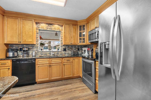 kitchen with dark stone countertops, sink, light wood-type flooring, stainless steel appliances, and a textured ceiling