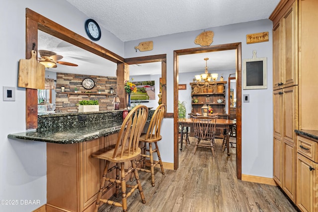 interior space with decorative backsplash, dark stone countertops, wood-type flooring, a textured ceiling, and ceiling fan with notable chandelier